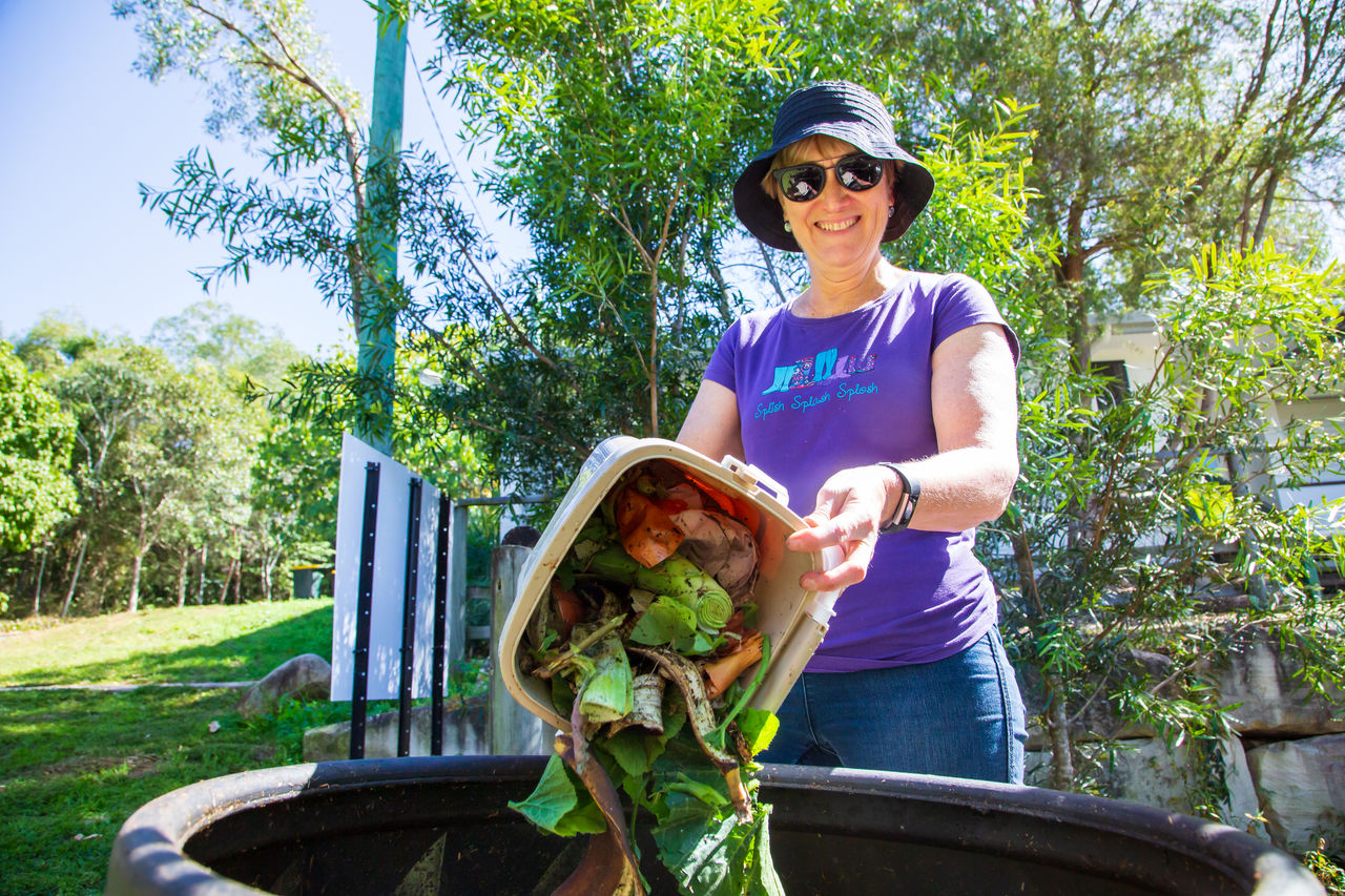 A woman adding food waste to a composting bin at a community garden.