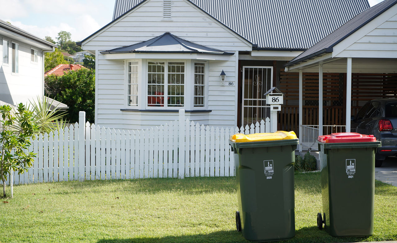 White post-war house with general waste bin and recycling bin on footpath.