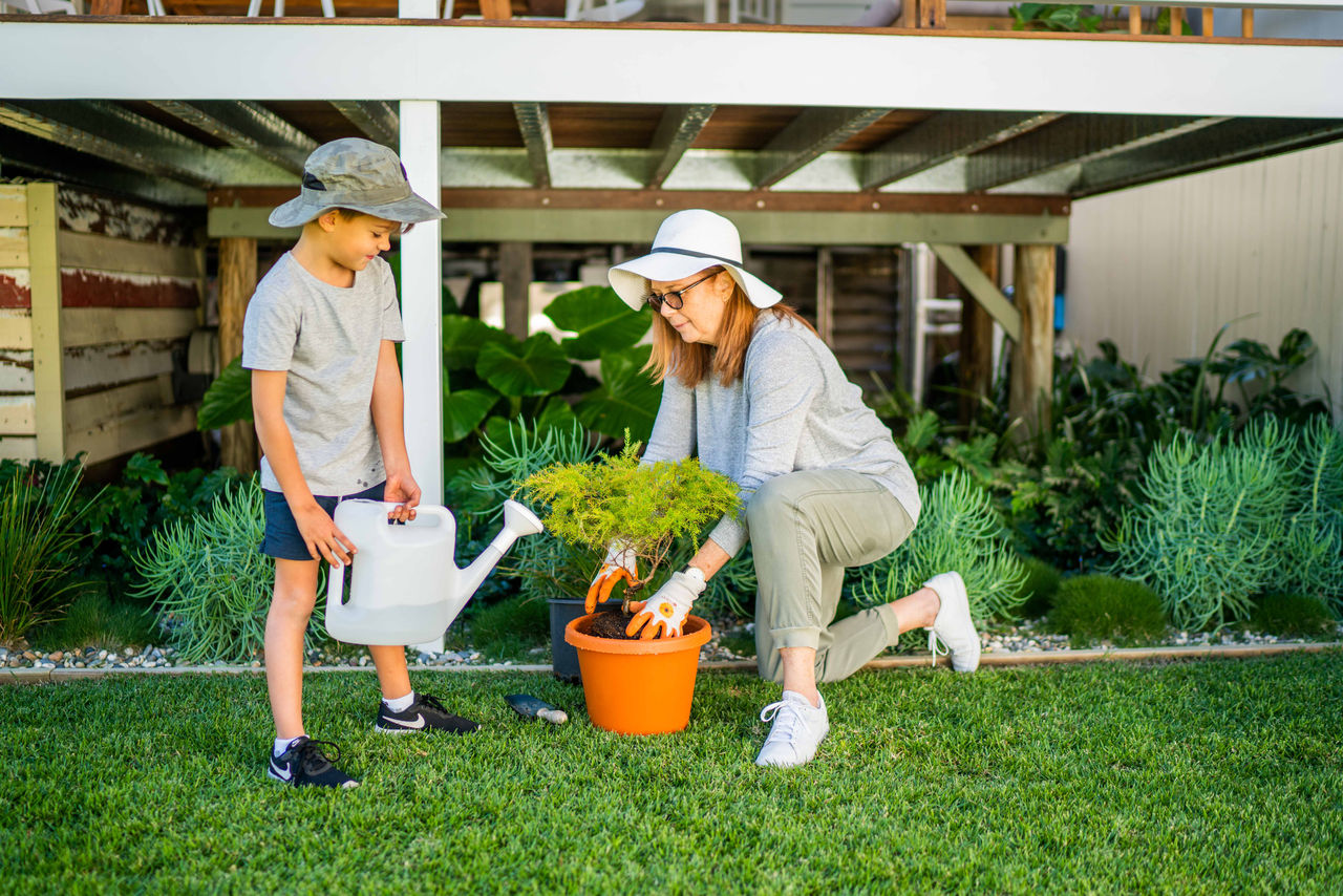 A woman and a boy planting a tree in a pot in the garden.
