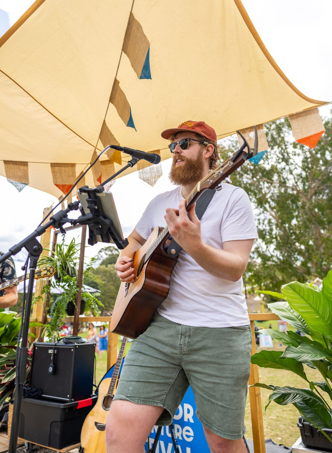 A person playing his guitar and singing into a microphone with sound equipment around him.