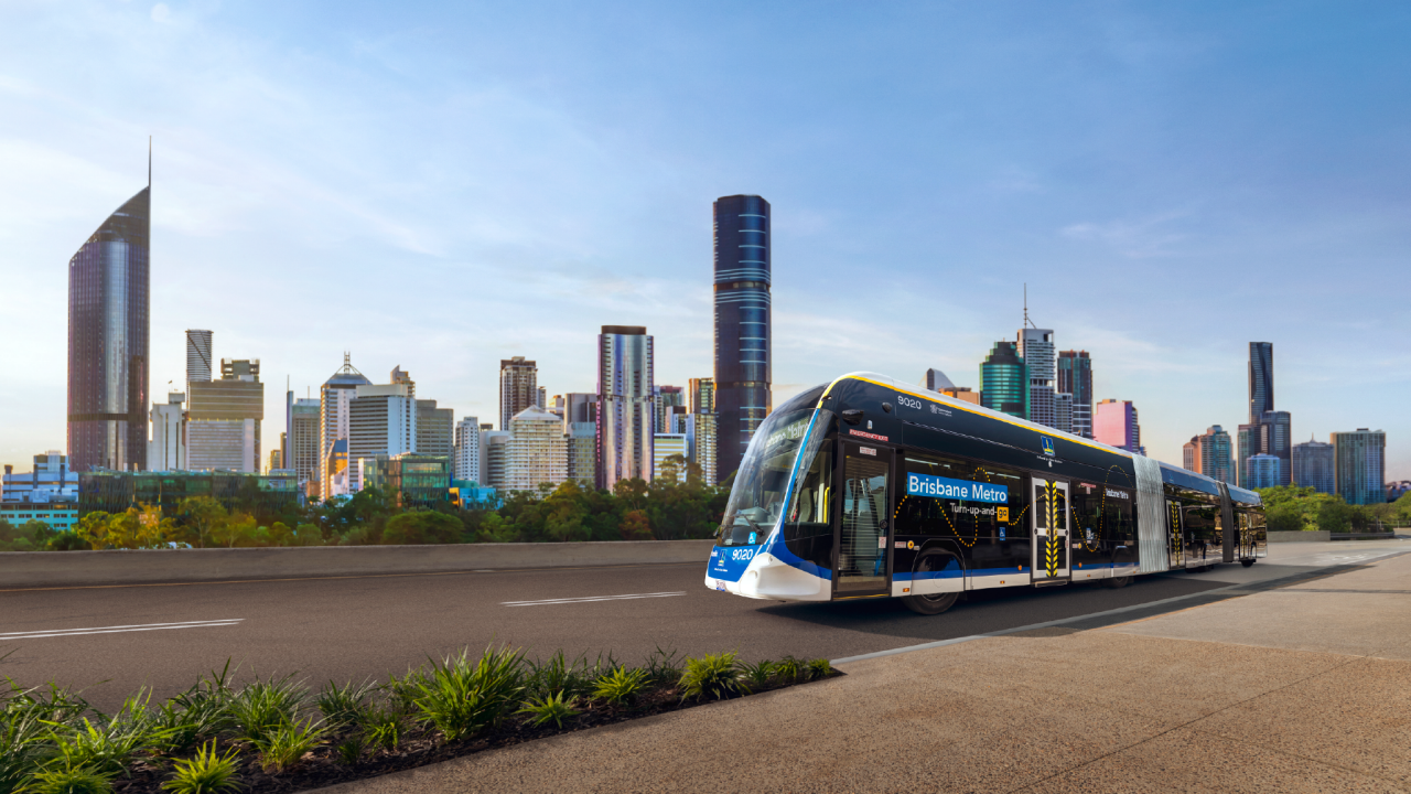 Brisbane Metro vehicle with '9020' on side and 'Brisbane Metro - Turn-up-and-go' on side. Brisbane CBD in background.