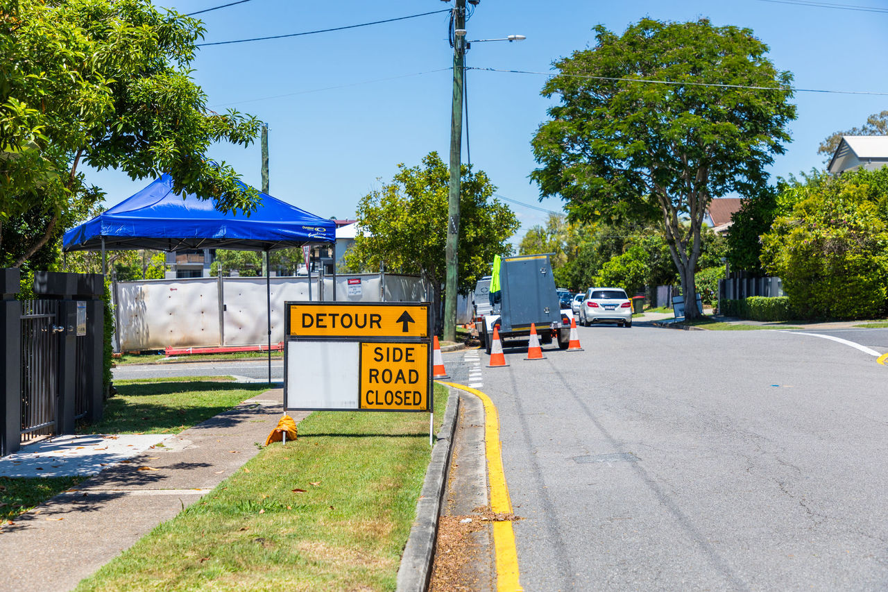Road closure sign saying 'Detour. Side road closed' on a suburban street.