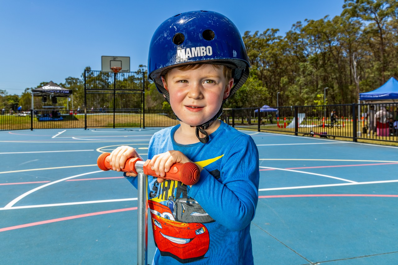 Young boy wearing a helmit while riding a scooter on a sports court