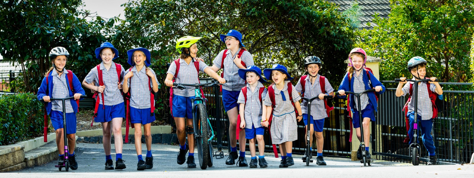 A group of children in school uniforms walking and riding scooters in a horizonal line