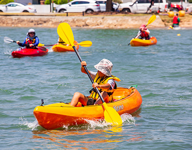 Young boy in a kayak paddling through water with other kayakers behind him