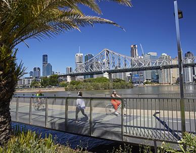 Cyclists and person walking along the Brisbane Riverwalk with the Story Bridge in the background